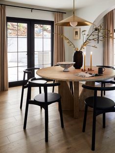 a dining room table with chairs and a vase on top of it, in front of a large window