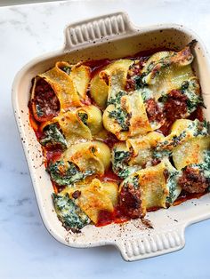 a casserole dish with spinach and sausage in it on a marble countertop