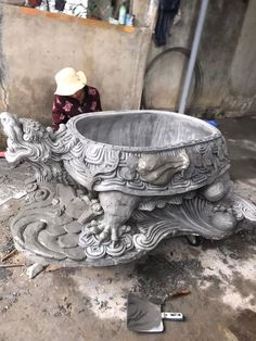 a woman sitting on the ground next to a large metal bowl with an elephant design