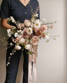 a woman in scrubs holding a bouquet of flowers and greenery with her hands