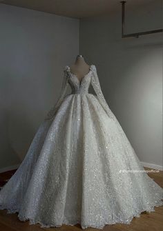 a white wedding dress with long sleeves on display in front of a wall and wooden floor