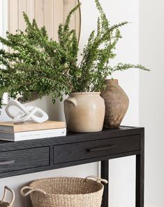 two vases with green plants on top of a black table next to a basket