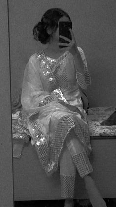 a woman sitting on a bench taking a selfie in front of her mirror wearing a dress with sequins