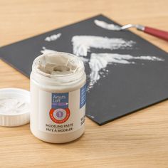 a jar of paint sitting on top of a table next to a piece of paper