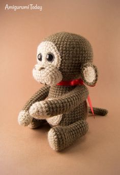 a crocheted stuffed monkey with a red ribbon around its neck sitting on a brown surface