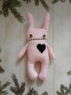 a pink stuffed animal with a black heart on it's face and eyes is hanging from a branch