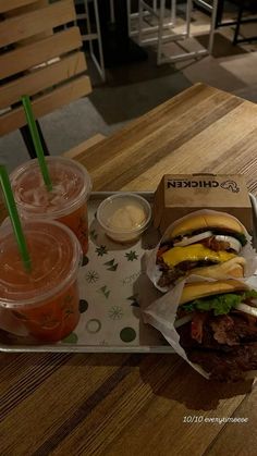 two sandwiches and drinks on a table at a fast food restaurant with wooden chairs in the background