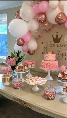 a table topped with lots of cakes and desserts covered in pink and white balloons