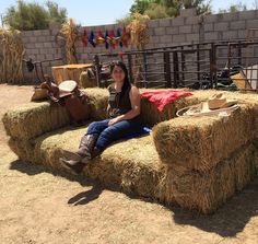 a woman sitting on hay bales with cowboy hats