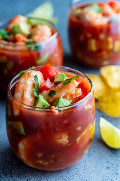 two glasses filled with food and garnished with cilantro, limes, and chips