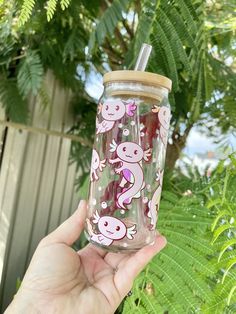 a hand holding up a pink and white glass cup with monkeys on it, in front of some green plants