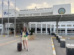 a woman standing in front of an airport with her luggage