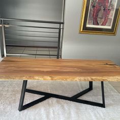 a wooden table sitting on top of a white rug next to a metal rail and framed painting