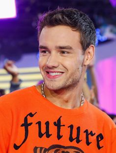 a man in an orange shirt smiles at the camera while wearing a necklace with a tiger on it