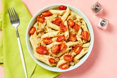 a bowl filled with pasta and tomatoes on top of a green napkin next to silverware