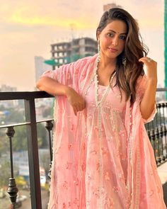 a woman in a pink dress standing on a balcony with her hand on her hip