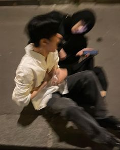 two people sitting on the ground and one is holding a cell phone in his hand