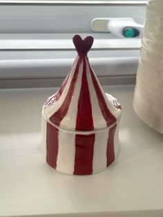 a red and white striped container sitting on top of a window sill next to a roll of toilet paper