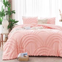 a bed with pink comforter and pillows in a room next to a plant on the floor