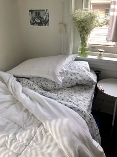 an unmade bed sitting next to a window with white sheets and pillows on it