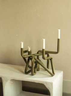 three candles sitting on top of a white table in front of a wall with no one around it