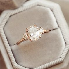 an engagement ring sitting on top of a velvet cushion in a white and gold box