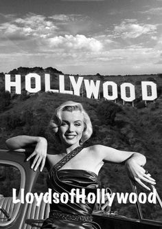 a black and white photo of a woman leaning on the hood of a car with hollywood sign in the background