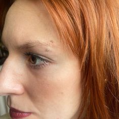 a close up of a woman with red hair and piercings on her nose looking at the camera