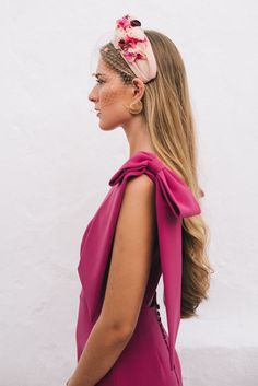 a woman with long hair wearing a pink dress and flower in her hair, looking off to the side