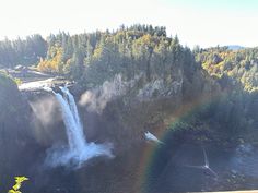 a waterfall with a rainbow in the middle and trees around it, on a sunny day