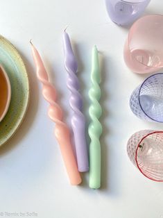 three candles sitting on top of a table next to a cup and saucer with spoons