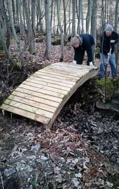 two people standing on a wooden bridge in the woods