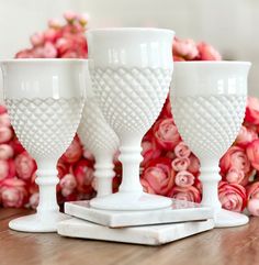 three white goblets sitting on top of a wooden table next to pink flowers