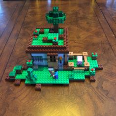 a toy house made out of legos on a wooden floor with a table in the background