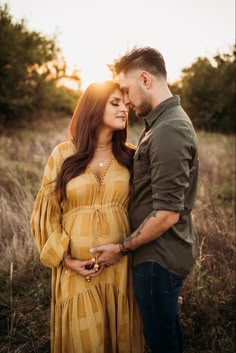 a pregnant couple standing in the grass at sunset