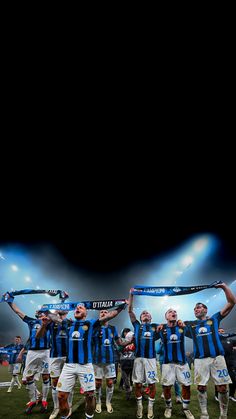 a group of men standing on top of a soccer field holding up a blue and white scarf