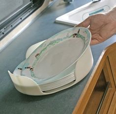 a person holding onto a stack of plates on top of a kitchen counter next to a sink