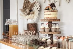 a table topped with lots of cupcakes next to glasses filled with liquid and pine cones