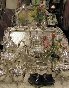 a table topped with lots of silver dishes and vases on top of each other