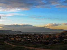 the sun is setting over some hills and mountains in the distance, as seen from an overlook