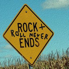 a yellow rock and roll never ends sign sitting in the middle of a corn field