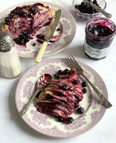 two plates topped with blueberry cheesecake next to a jar of jelly and spoons