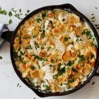 a skillet filled with pasta and cheese on top of a white table next to some parsley