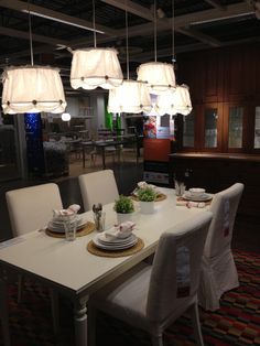 a dining room table with white chairs and lights hanging from the ceiling