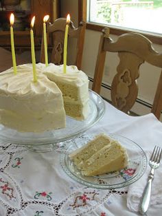 a cake with white frosting and lit candles sits on a table in front of a window