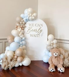 a teddy bear sitting on top of a wooden floor next to balloons and a sign