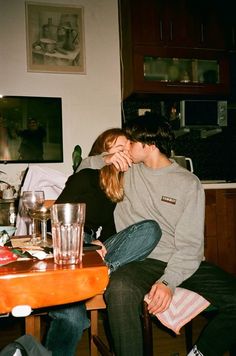 two people sitting at a table kissing each other