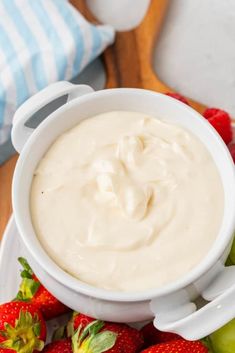 a white bowl filled with cream next to some strawberries and an apple on a plate