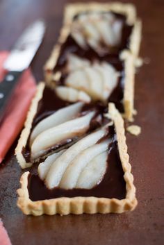 two slices of chocolate apple tart sitting on top of a table next to a knife