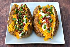 four baked potatoes with toppings on a white plate